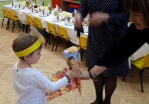 Pani dyrektor razem z wychowawczynią wręczają dziewczynce rożek ze słodyczami.